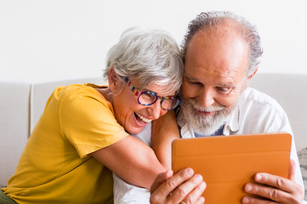 Gutgelaunte Senioren relaxen mit Tablet auf Sofa